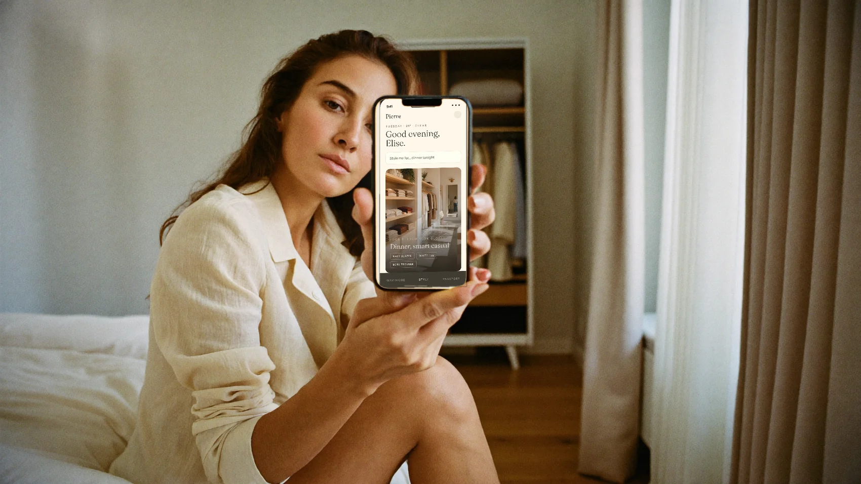 A woman at home holding her phone, the Pierre app showing a look styled from her own closet.